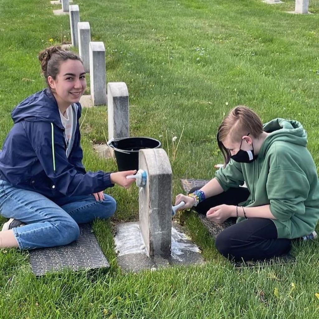 students cleaning cemetery head stone