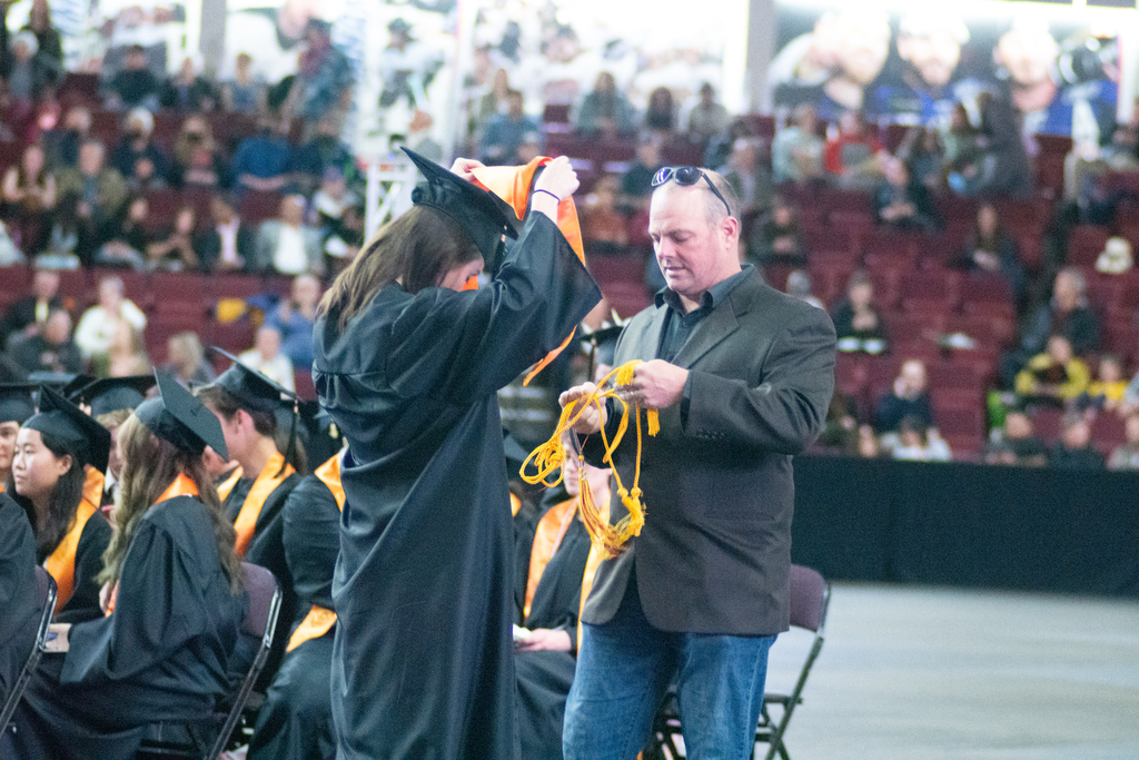 father assists daughter with cap and gown at graduation