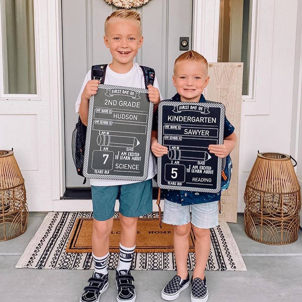 two young boys standing on porch with first day of school sign
